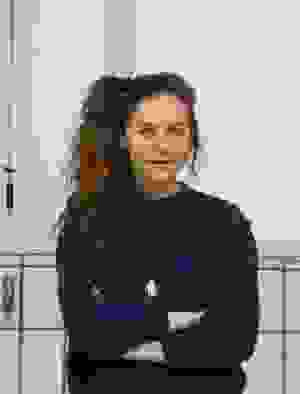 Junge Frau mit blauem Pulli und braunem Zopf verschließt ihre Arme.