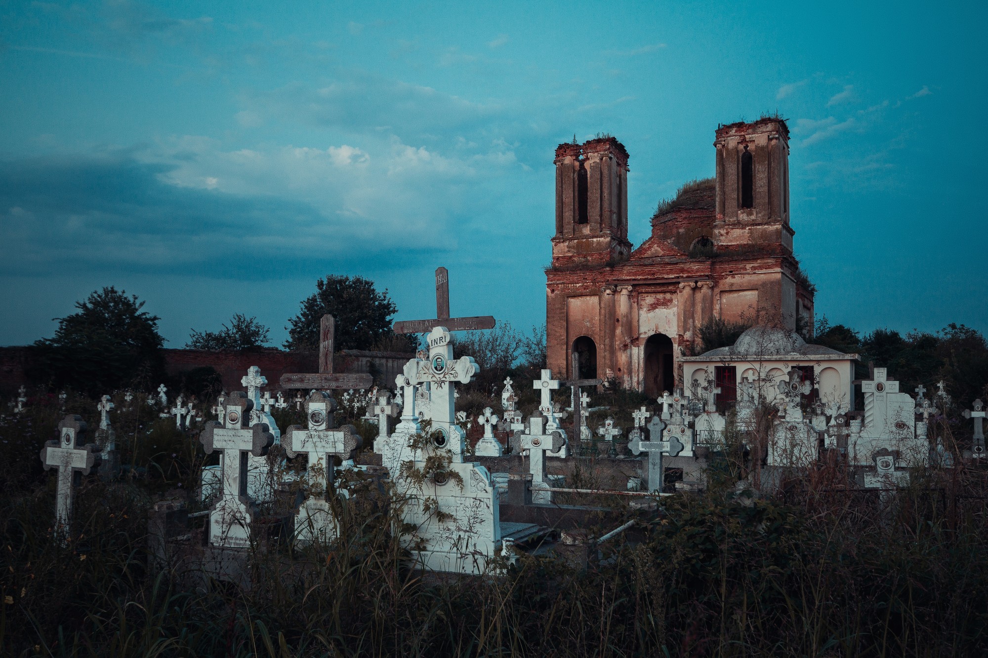 Fotografie einer bemoosten Kirchen-Ruine, die hinter weißen Grabsteinen steht.