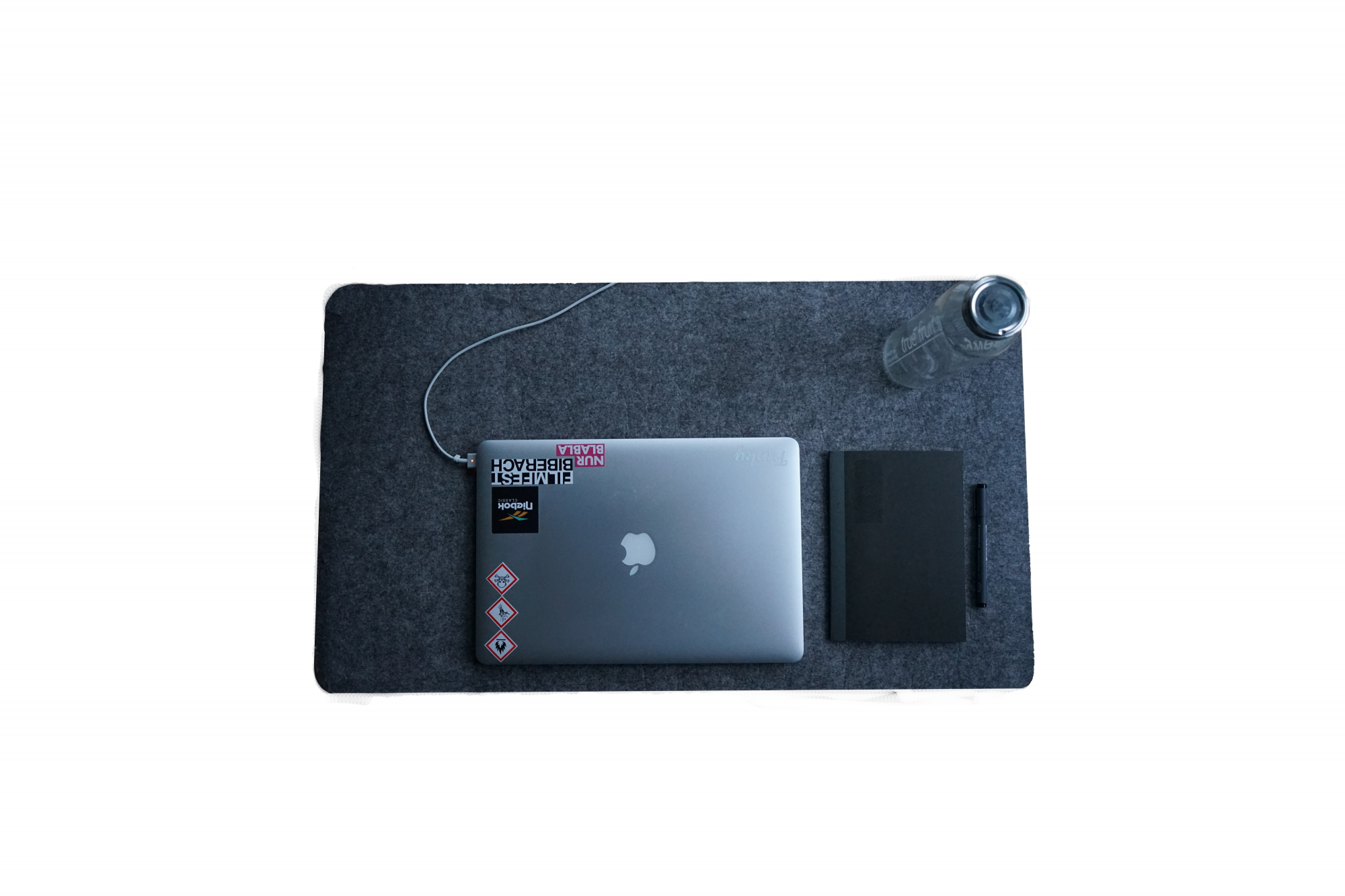 Zu sehen ist eine graue Matte mit einem Laptop, einer Flasche, sowie ein schwarzes Notitzbuch und ein Stift.